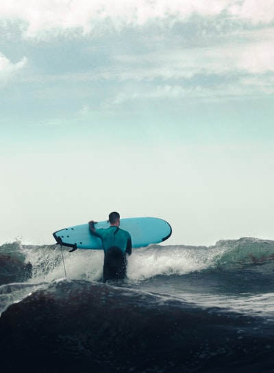 白天，穿着蓝色潜水服的男子在海边举着蓝色冲浪板